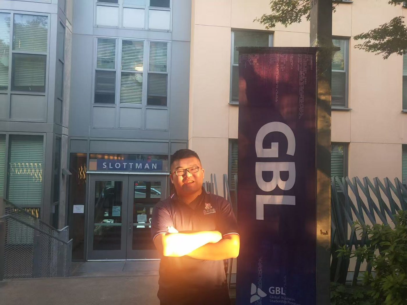 Nathan in front of Slottman Hall with a GBL banner